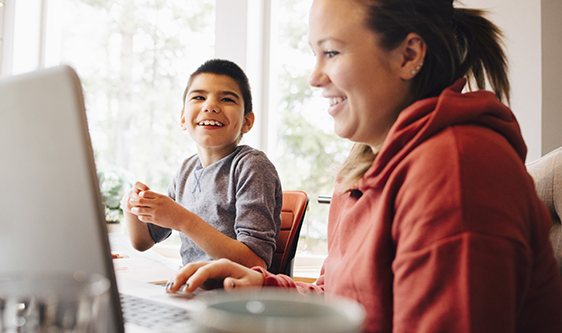 Mother using laptop while sitting with happy autistic son in living room at home
