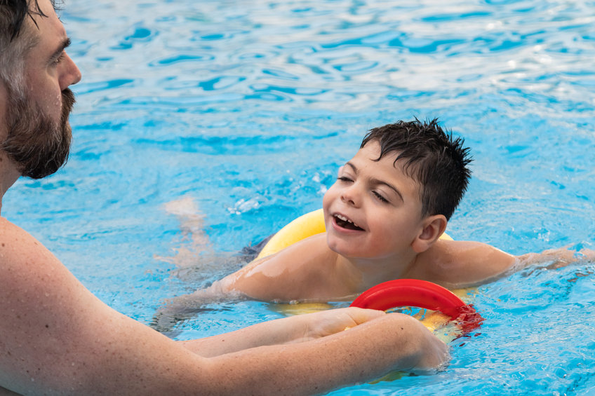 disabled boy with a float laughs as he plays and swims in a pool with his father
